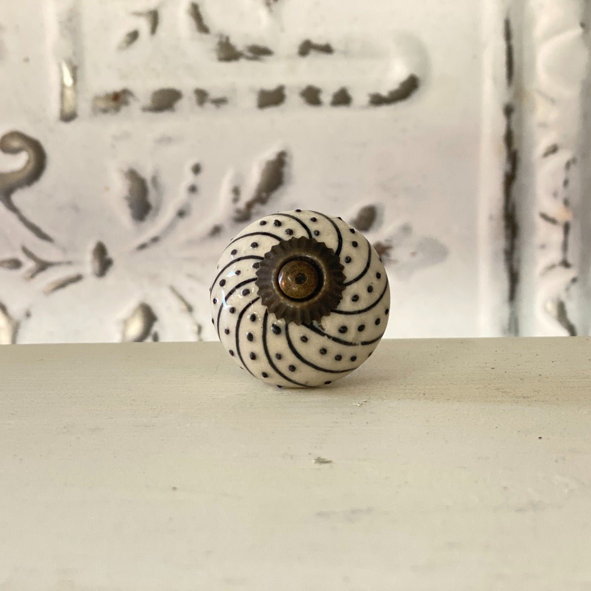 A black and white spiral patterned furniture knob with a visible center fastening mechanism, placed against a textured background.