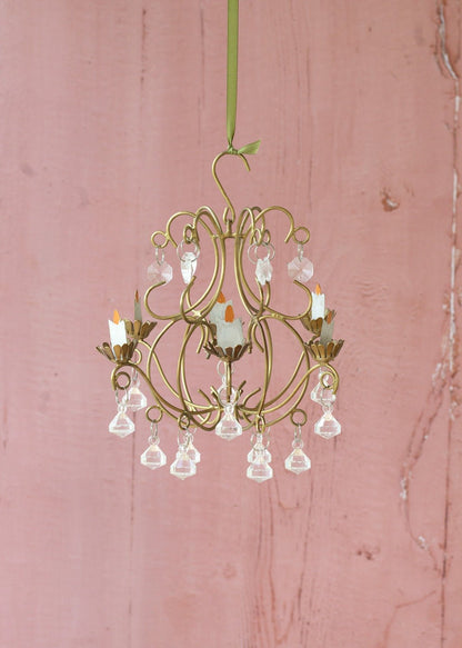Small gold chandelier with crystal accents on a pink wooden background
