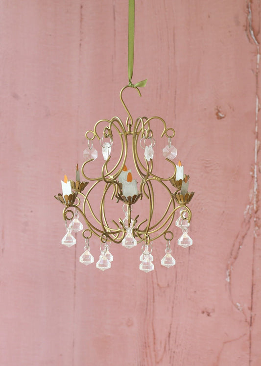 Small gold chandelier with crystal accents on a pink wooden background