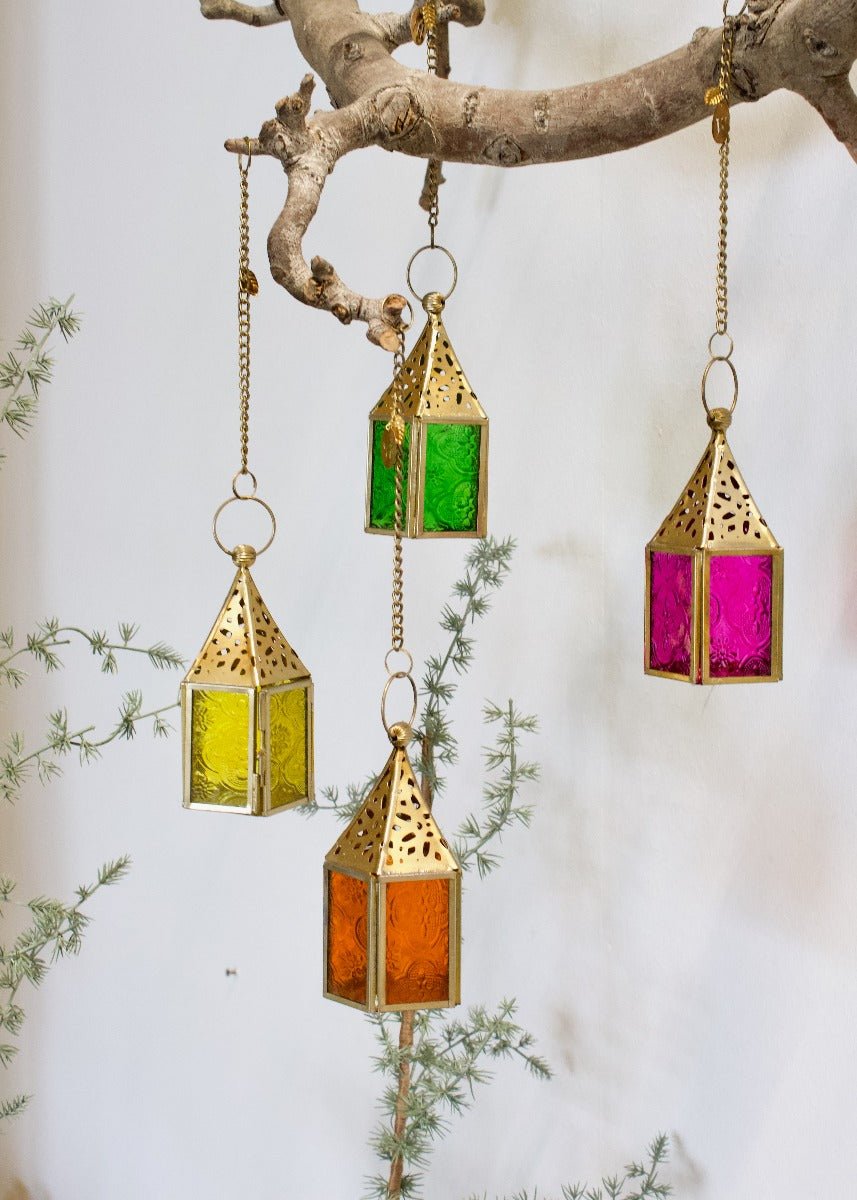Set of colorful brass lantern hangers with green, yellow, orange, and pink glass panels, hanging from a branch.