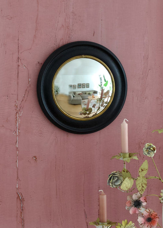 Round convex mirror with black frame on a pink wall with floral decorations.