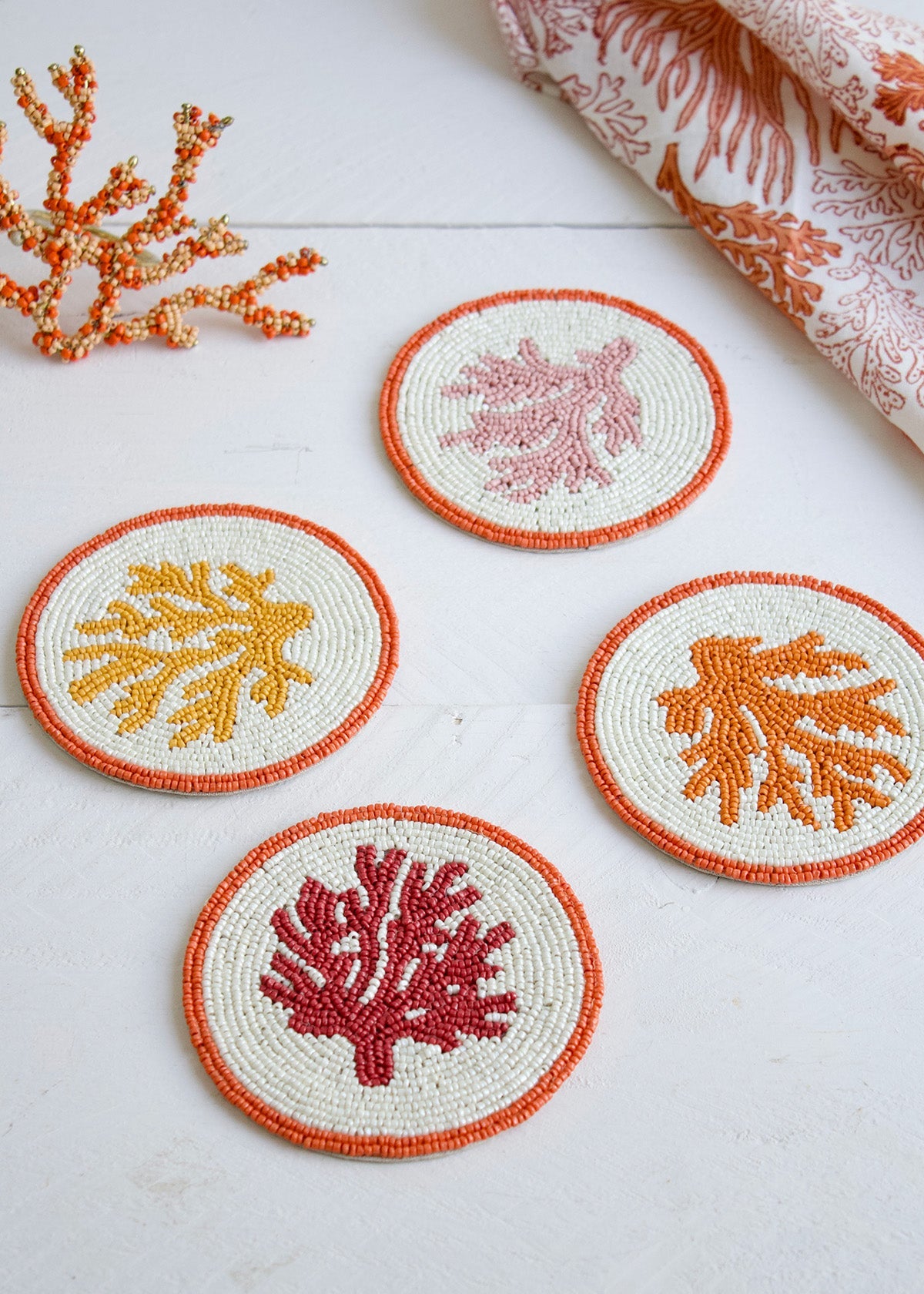 Set of four coral-themed coasters on a white surface with decorative fabric and coral decorations.