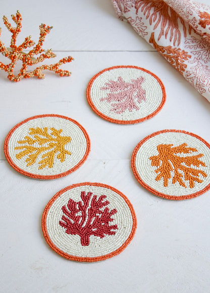 Set of four coral-themed coasters on a white surface with decorative fabric and coral decorations.