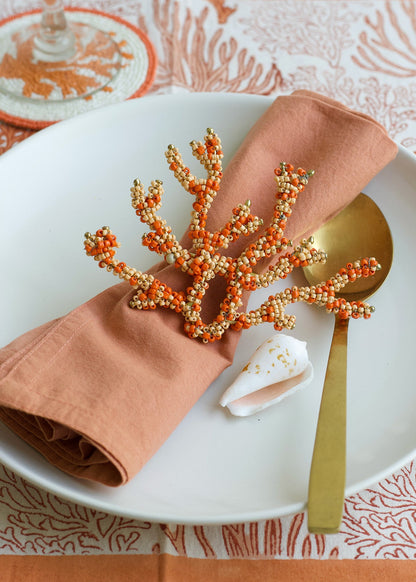 Decorative coral napkin ring on a peach napkin with a gold spoon on a white plate.