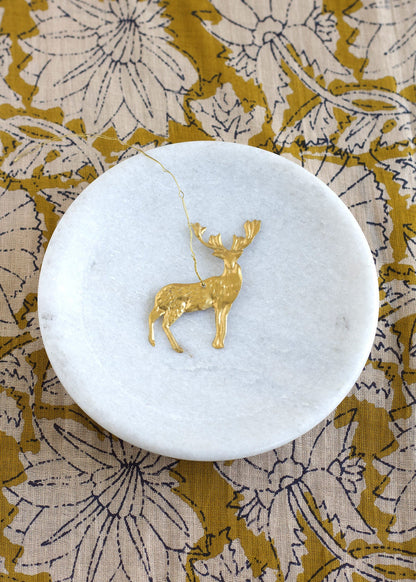 Gold deer pendant on a white marble coaster with a floral patterned fabric background