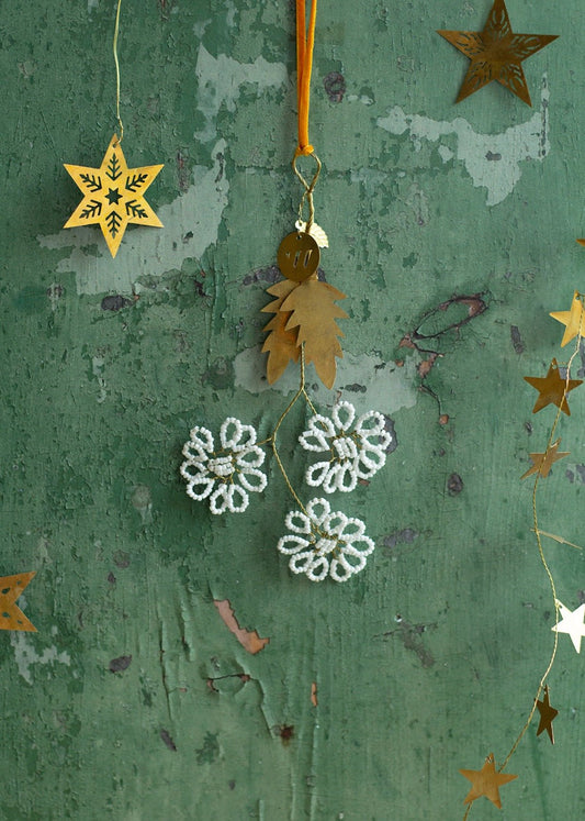 Gold brass ornament with three white beaded flowers on green textured background