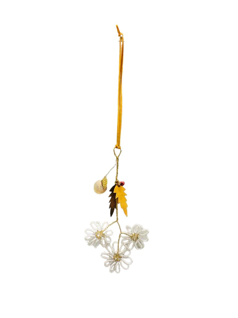 White beaded flower ornament with brass leaves and ochre ribbon on white background