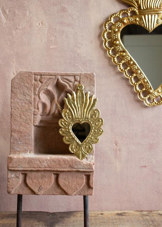 Decorative gold heart-shaped mirror on a stone surface with a pink wall background