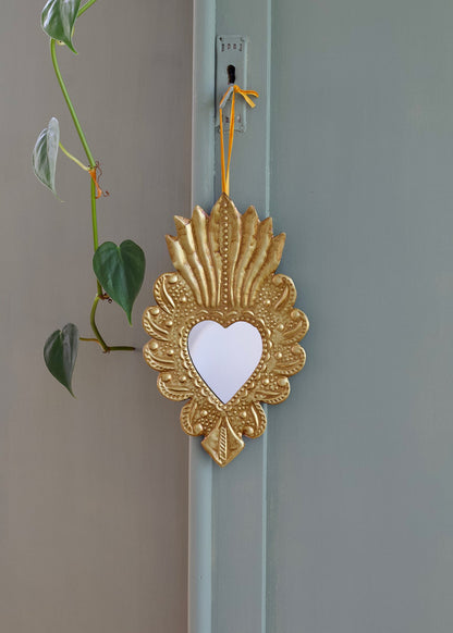 Decorative gold heart-shaped mirror hanging on a light blue door with a green plant in the background.