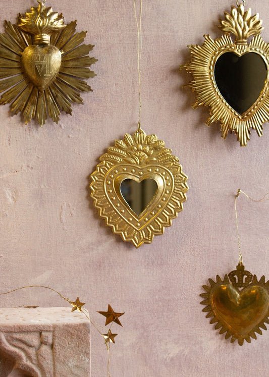 Golden handmade ex-voto heart mirror with embossed crown detail and dotted border, hanging on a wall.
