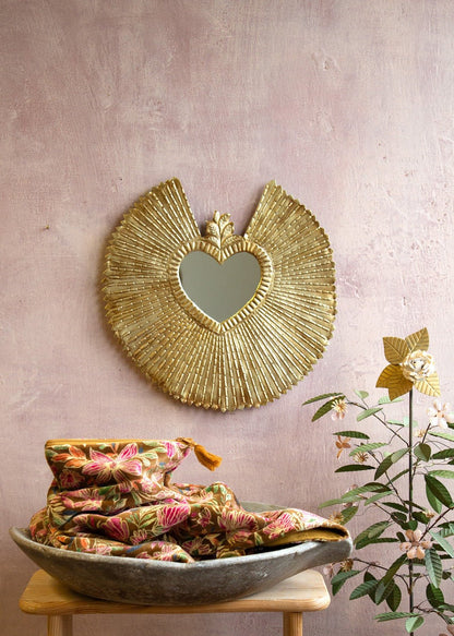 Ex-voto heart mirror with wide radiant golden frame on a pink wall.