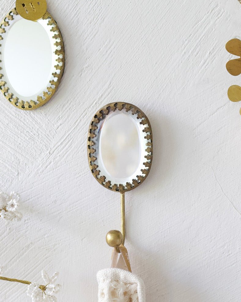 Handmade oval ex voto mirror hook with brass frame, styled on a wall with hanging towel and decorative brass elements.