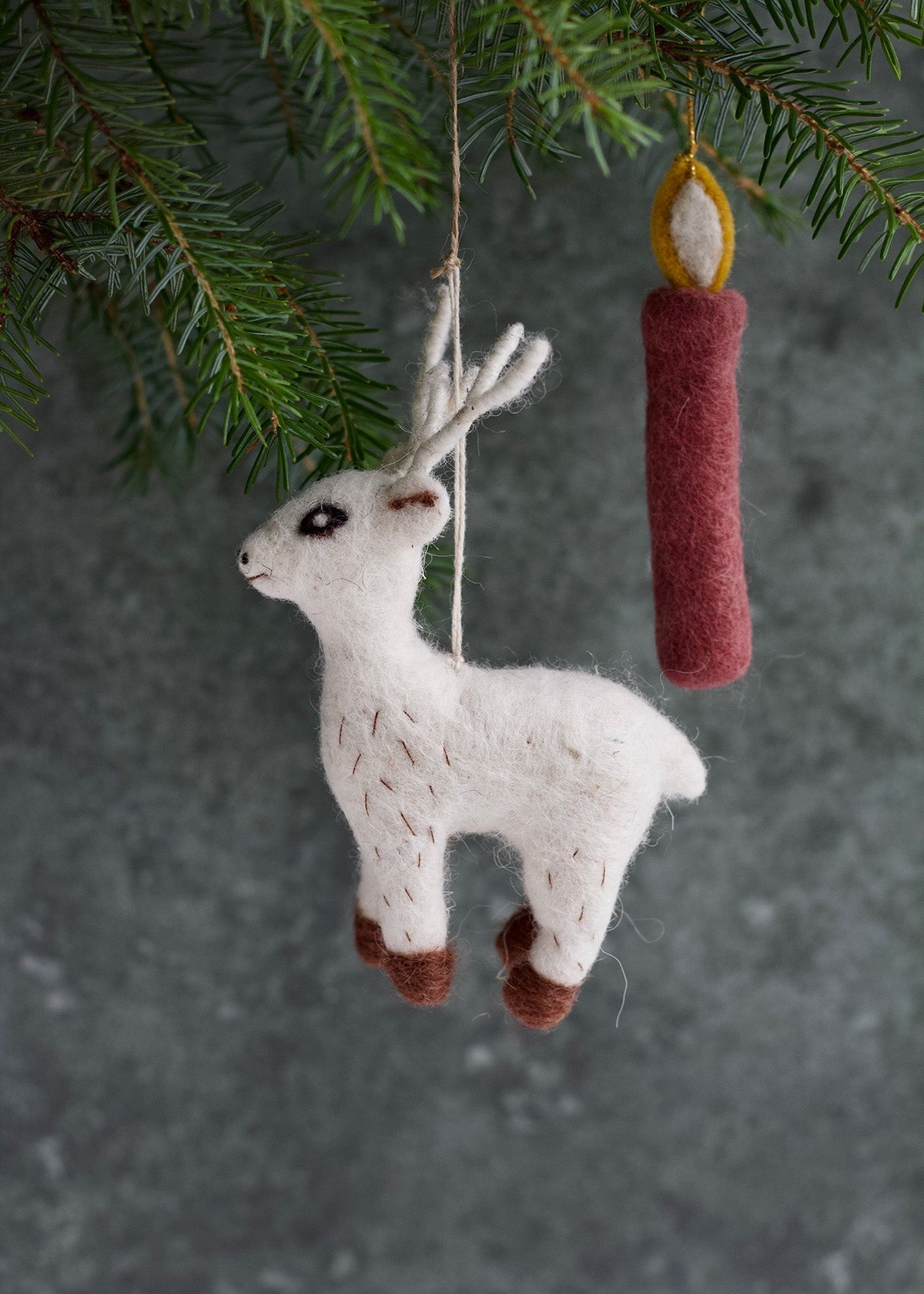 White felted animal ornament with brown accents hanging from a branch against a dark background.
