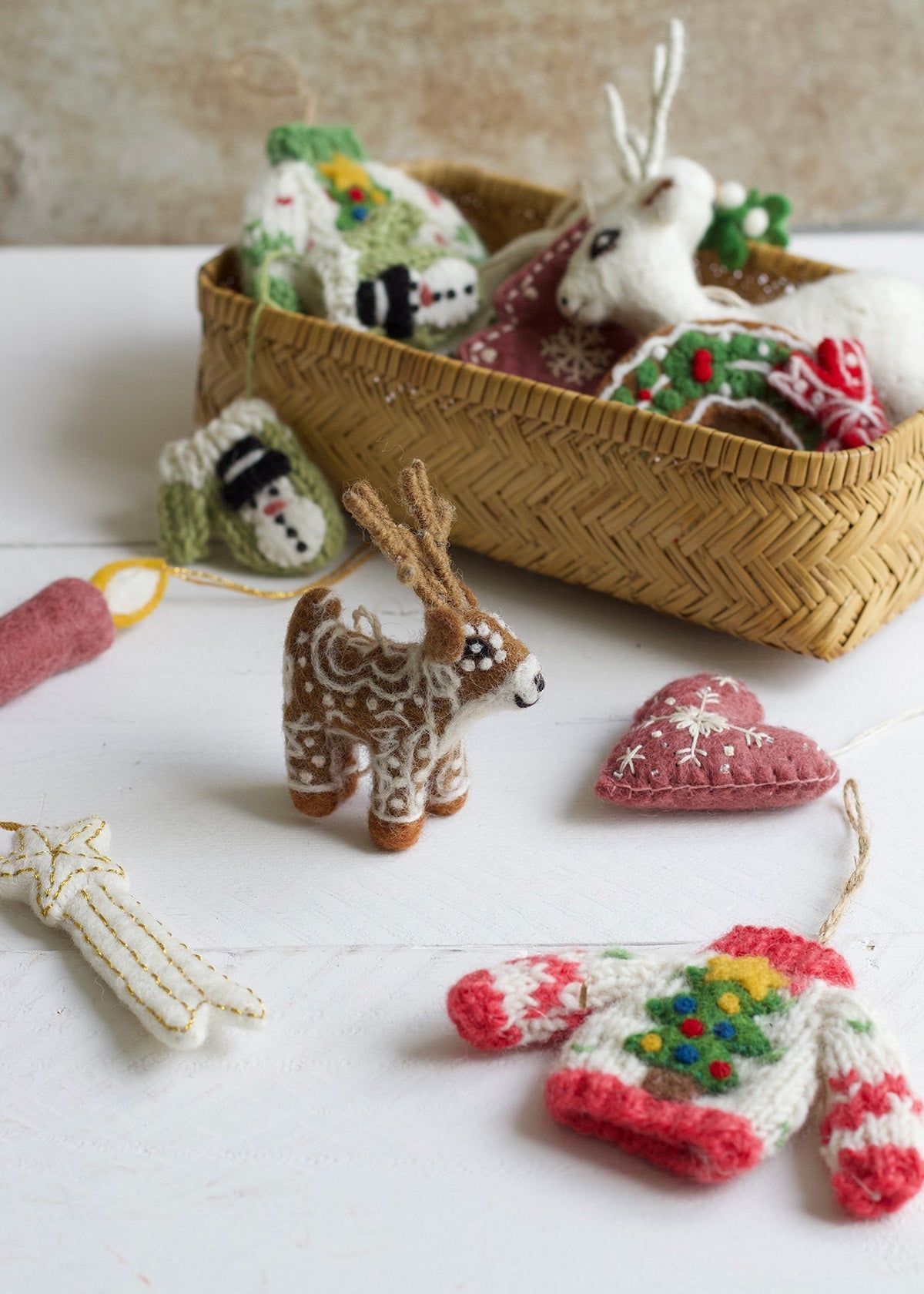 Collection of knitted and crocheted Christmas ornaments on a white surface with a woven basket.