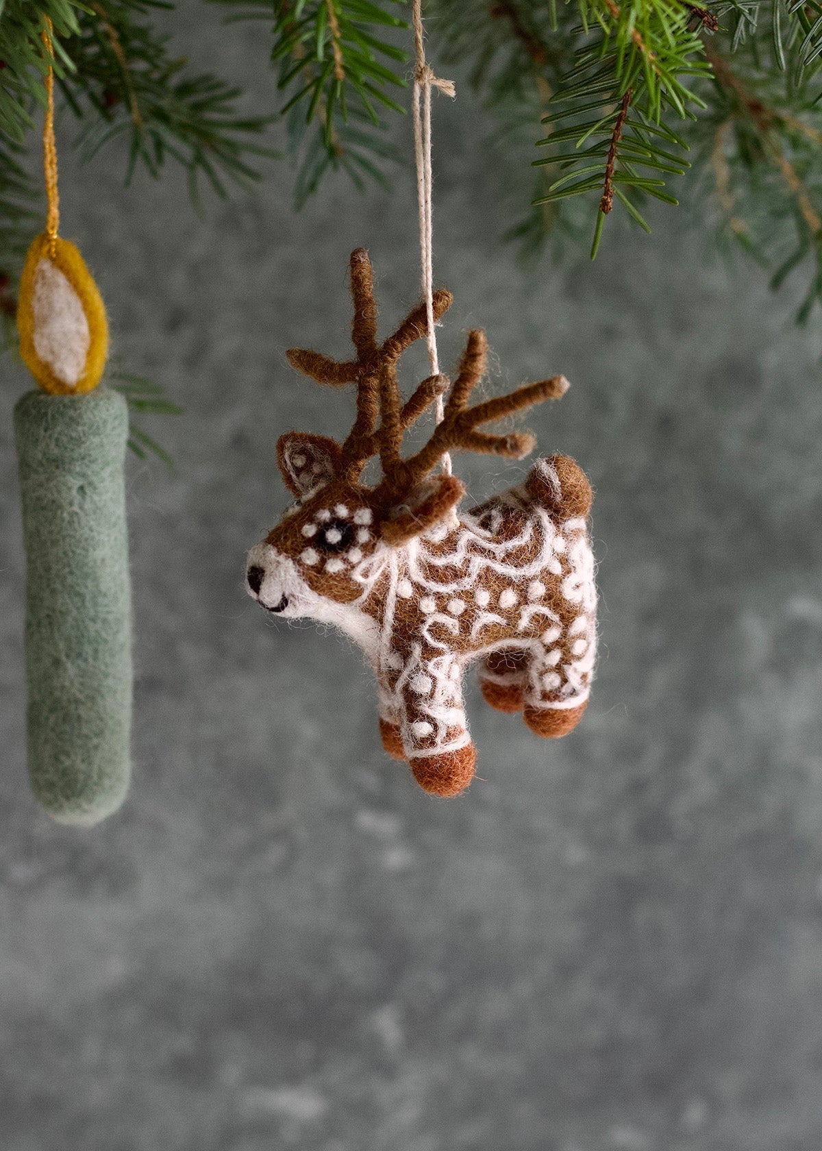 Felted reindeer ornament hanging from a branch with a gray background