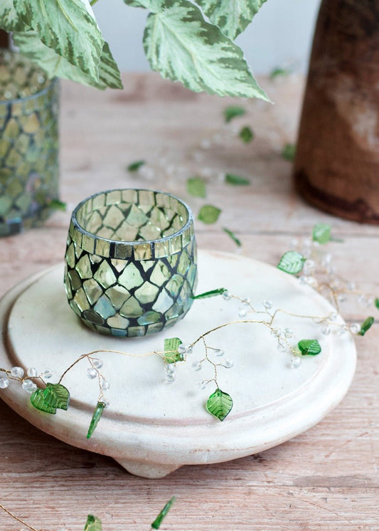 Garland with green glass leaves and clear beads on a golden wire, styled with a mosaic tealight holder on a round ceramic pedestal.