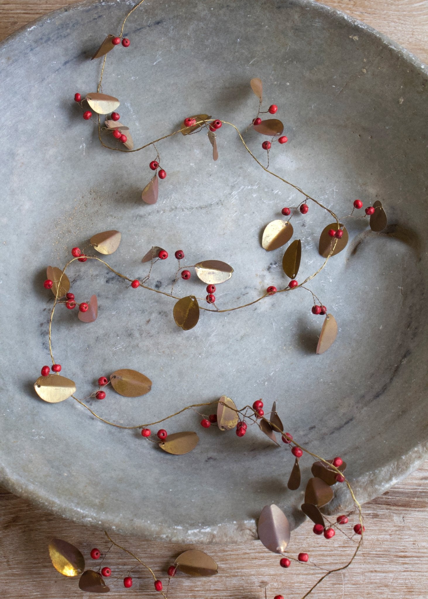 Decorative garland with red berries and gold leaves on a stone surface