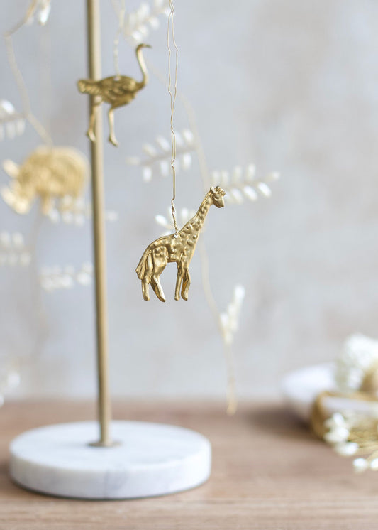 Brass giraffe ornament hanging from a decorative garland with soft white accents, displayed on a marble base stand.