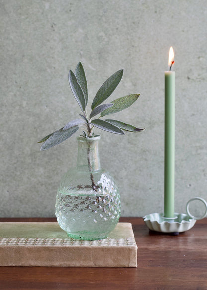 Vase with plant and candle on a wooden surface