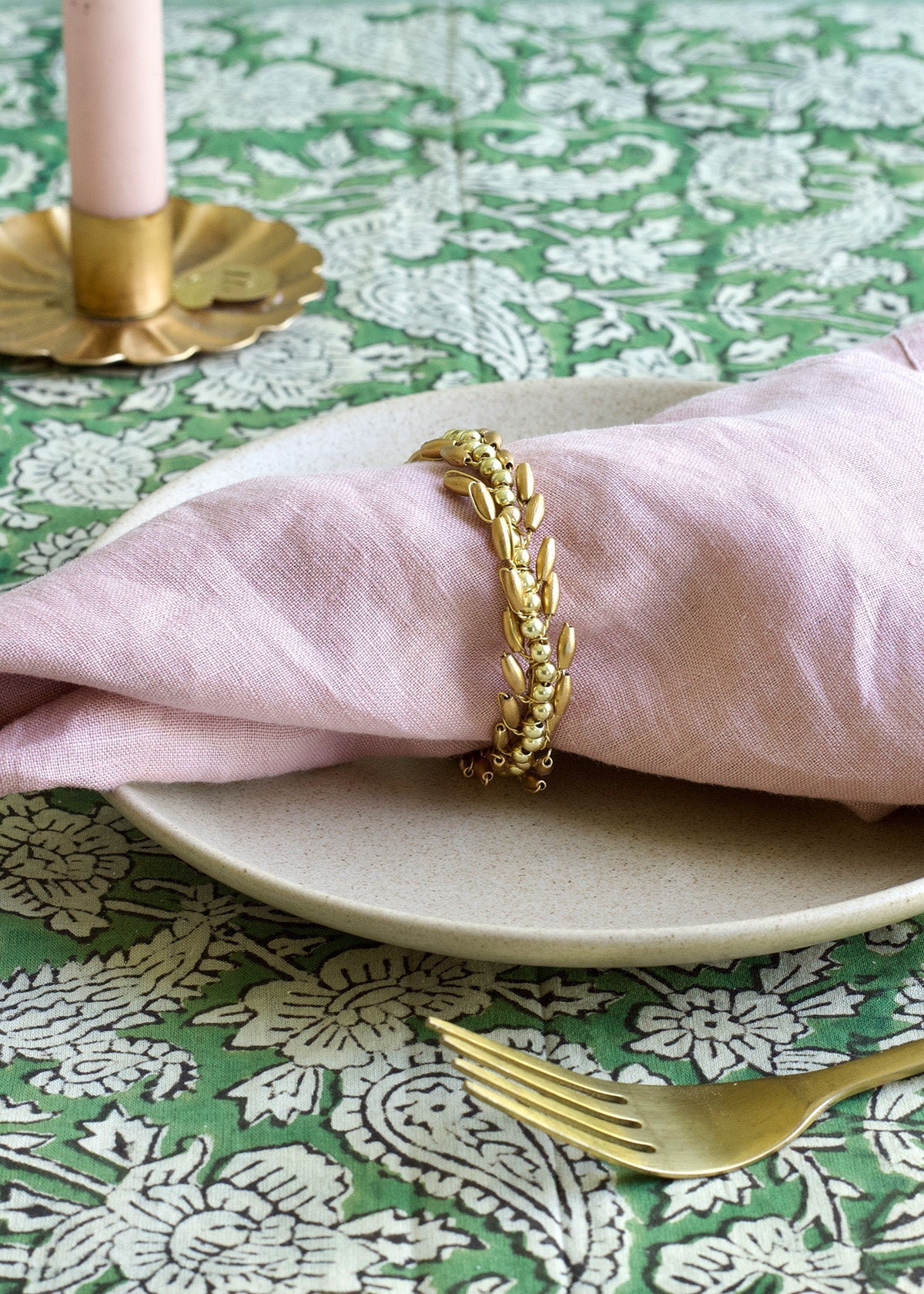 Gold napkin ring on a pink napkin with a green floral tablecloth