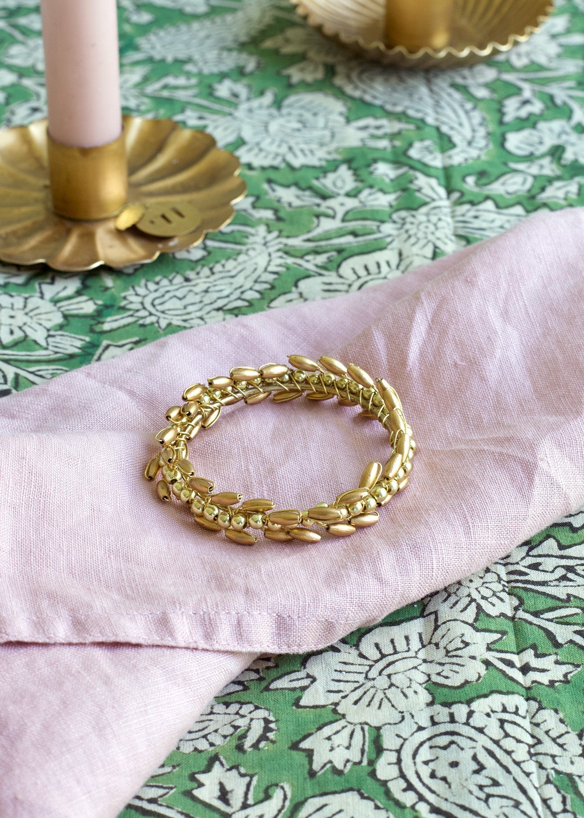 Gold bracelet on a pink fabric with a green patterned tablecloth