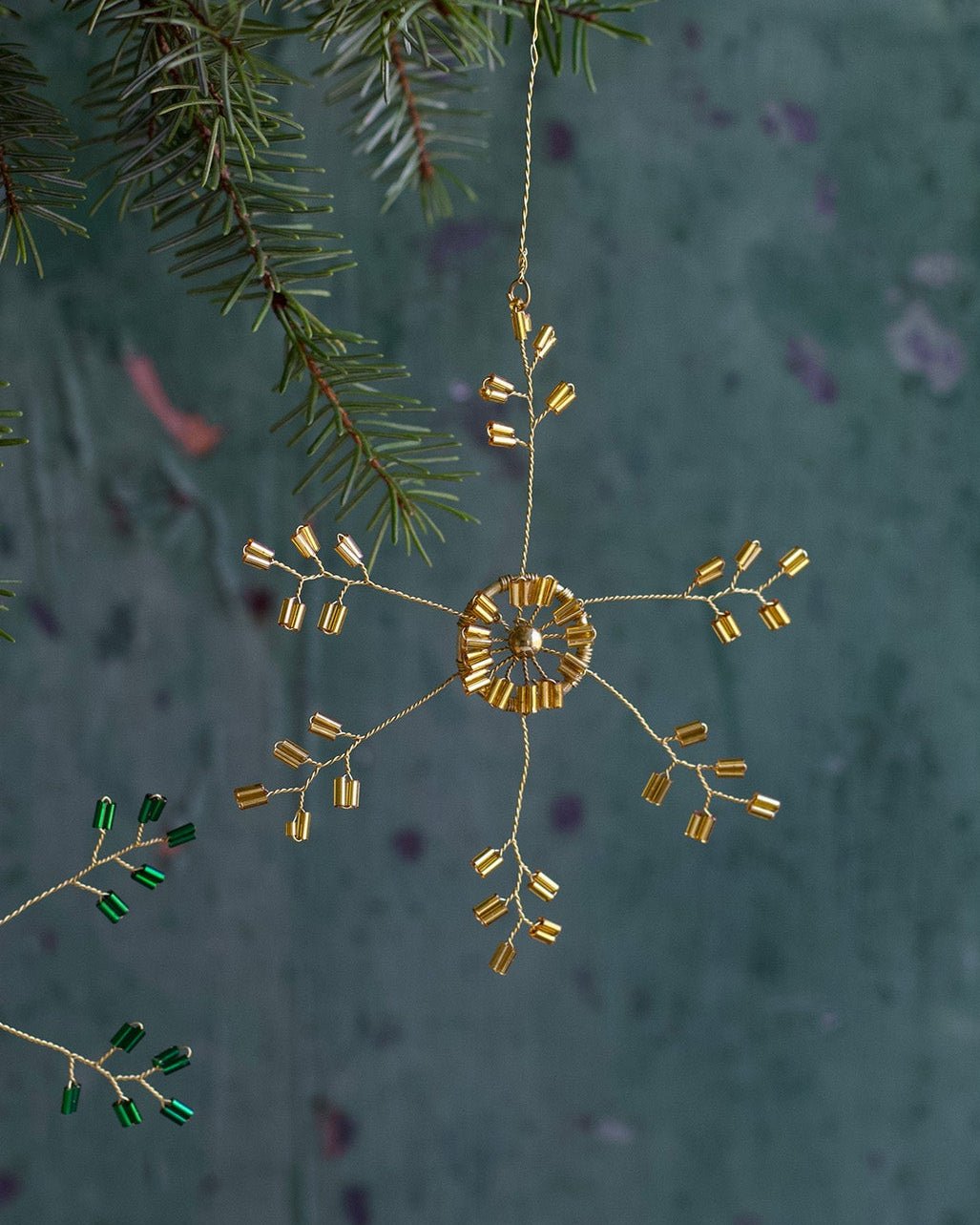 Decorative gold snowflake ornament hanging from a branch with a textured green background