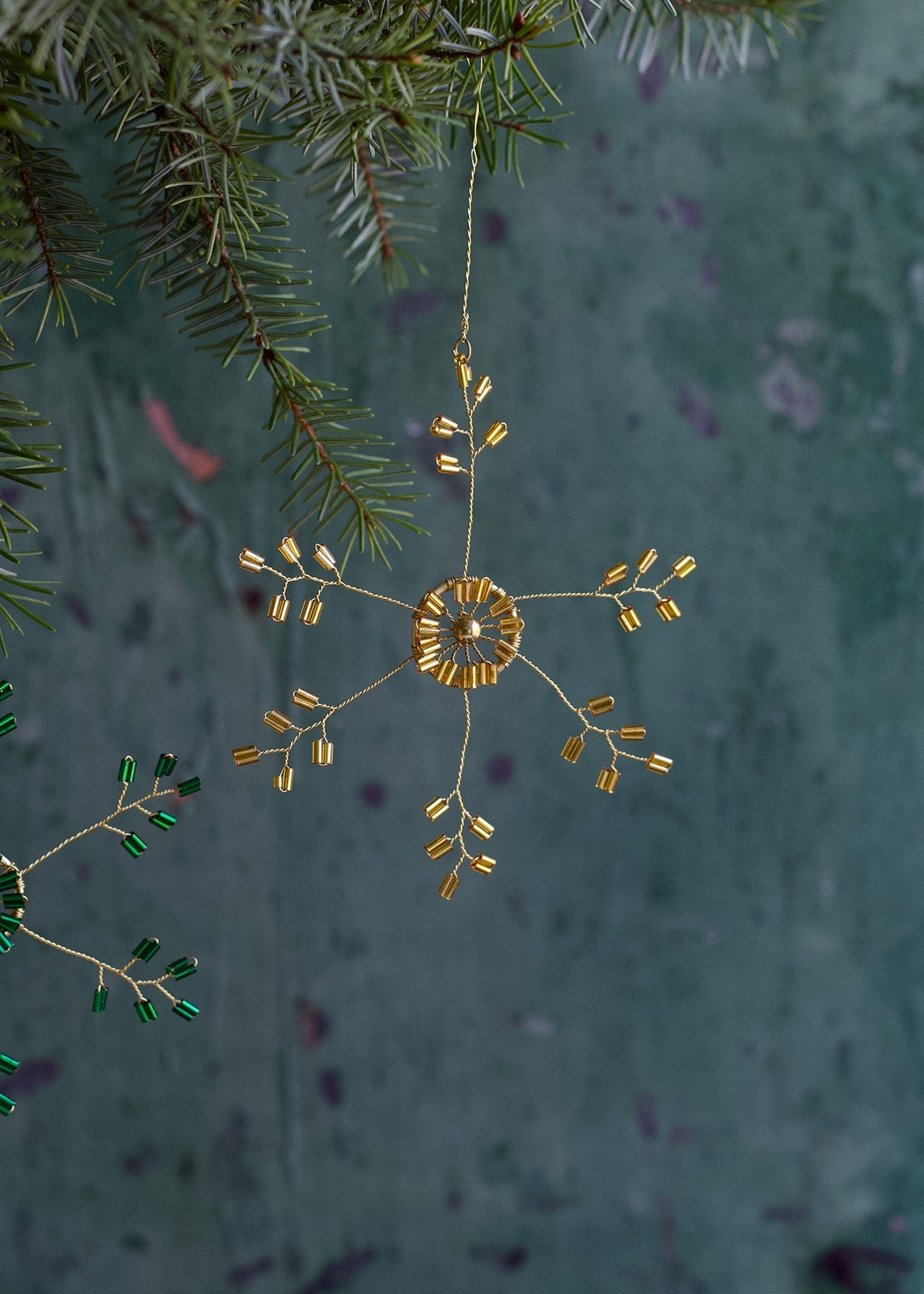 Decorative gold snowflake ornament hanging from a branch against a textured green background