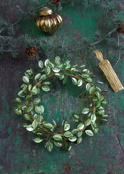 Green beaded leaf wreath with golden wire base styled on a rustic green surface.