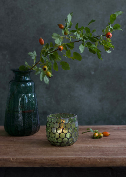 Decorative green vase with a candle and a branch with berries on a wooden surface.