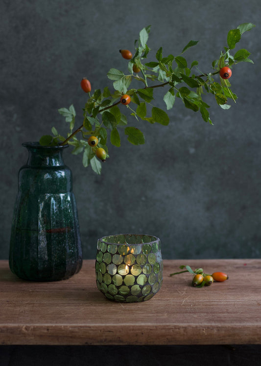 Decorative green vase with a candle and a branch with berries on a wooden surface.