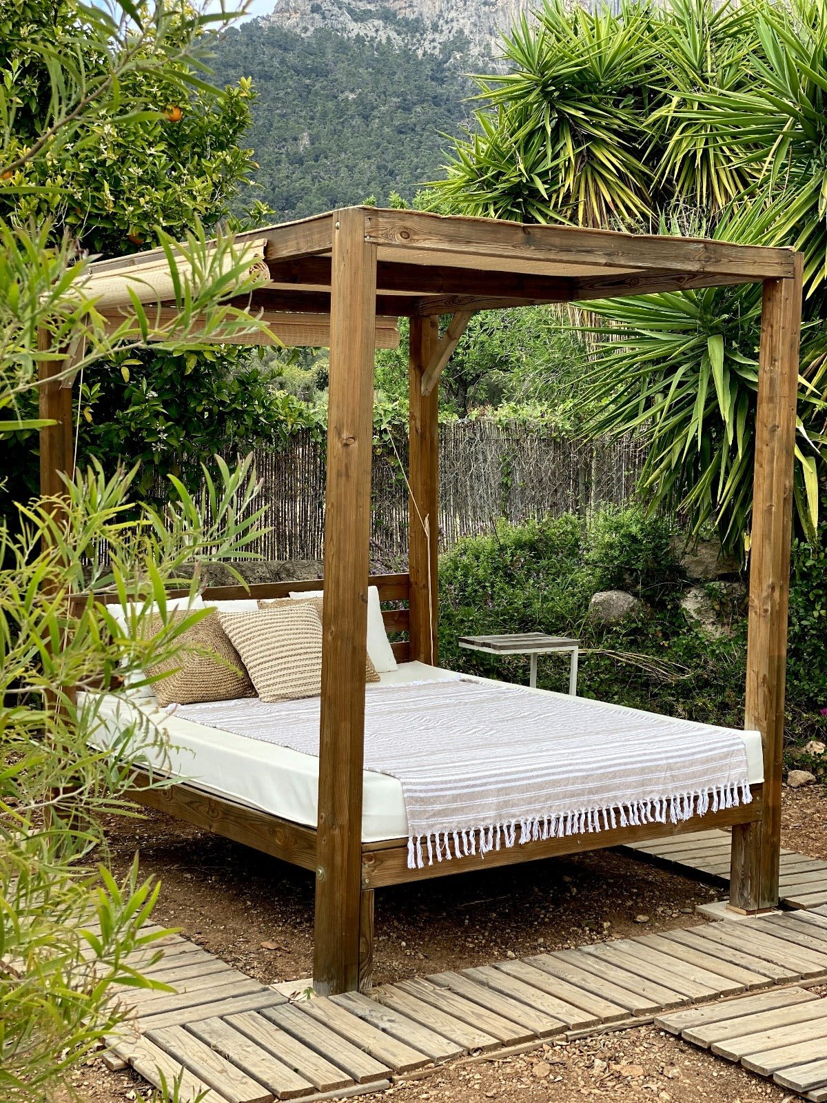 Wooden canopy bed in a garden setting with greenery and mountains in the background
