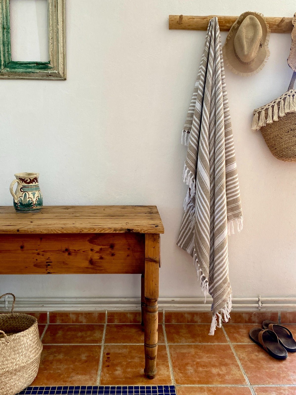 Wooden bench with a striped towel, hat, and pitcher against a white wall.