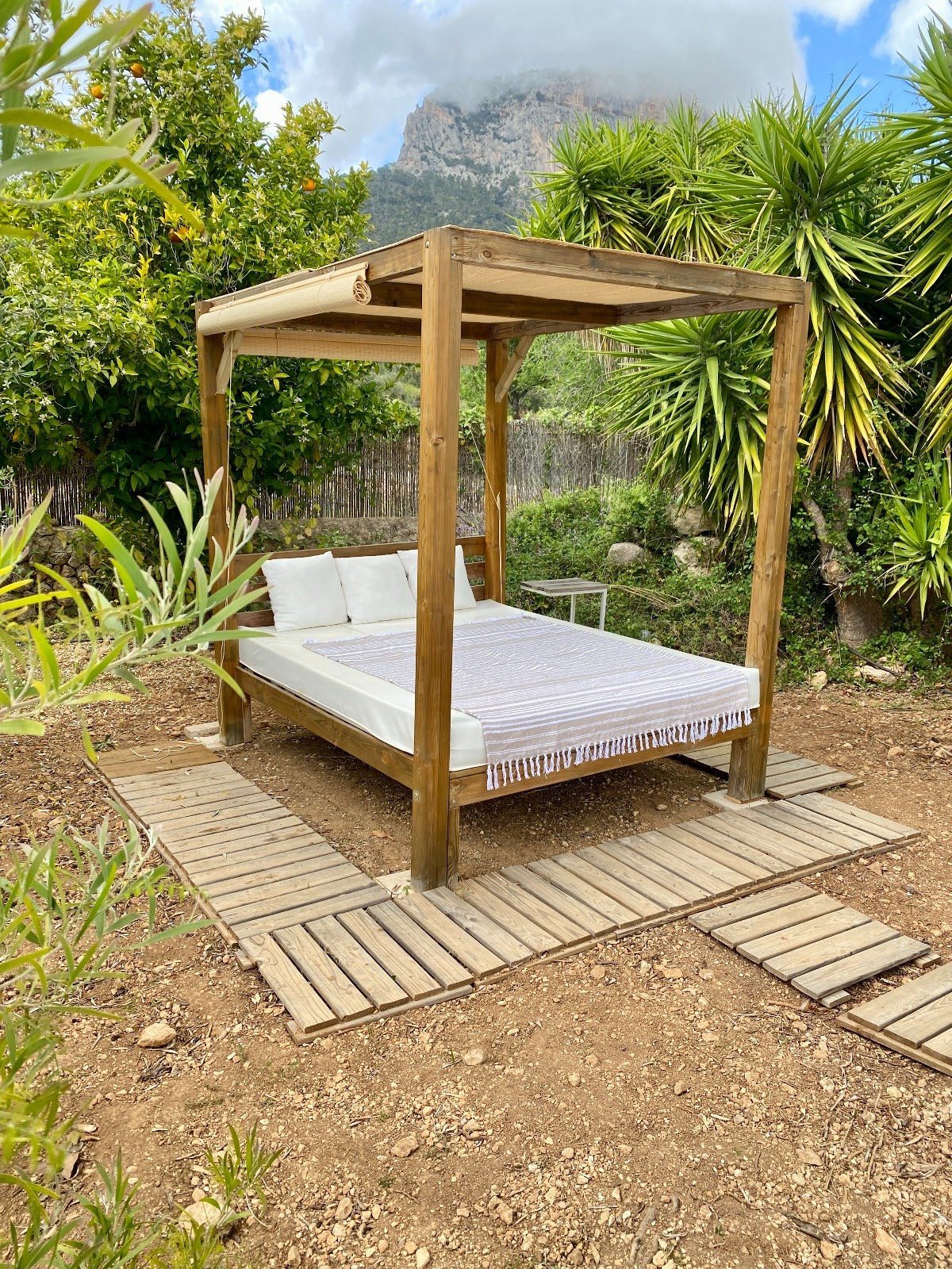 Wooden canopy bed in a garden setting with greenery and mountains in the background