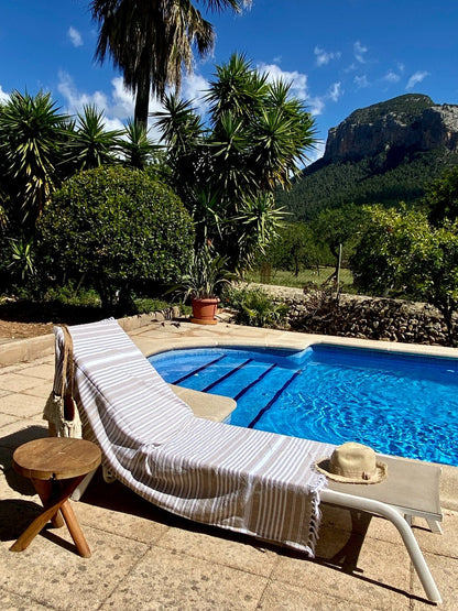Chaise lounge by a pool with mountains in the background, sunbathing bed with a striped towel