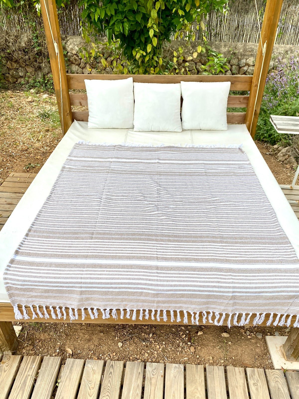 Bed with white bedding and a striped coverlet under a wooden canopy in an outdoor setting.