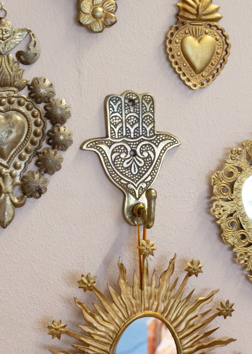Brass colored metal wall hook with floral pattern hanging on a pink wall surrounded by other decorative ornaments