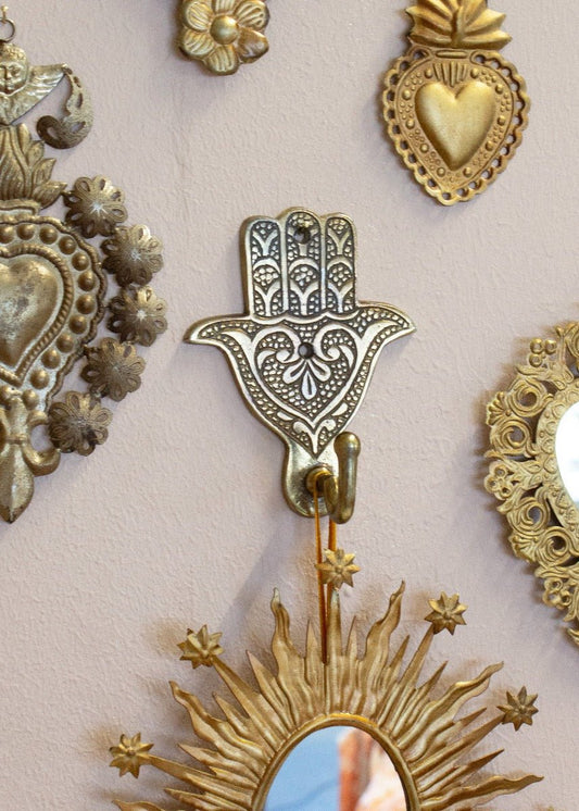 Brass colored metal wall hook with floral pattern hanging on a pink wall surrounded by other decorative ornaments
