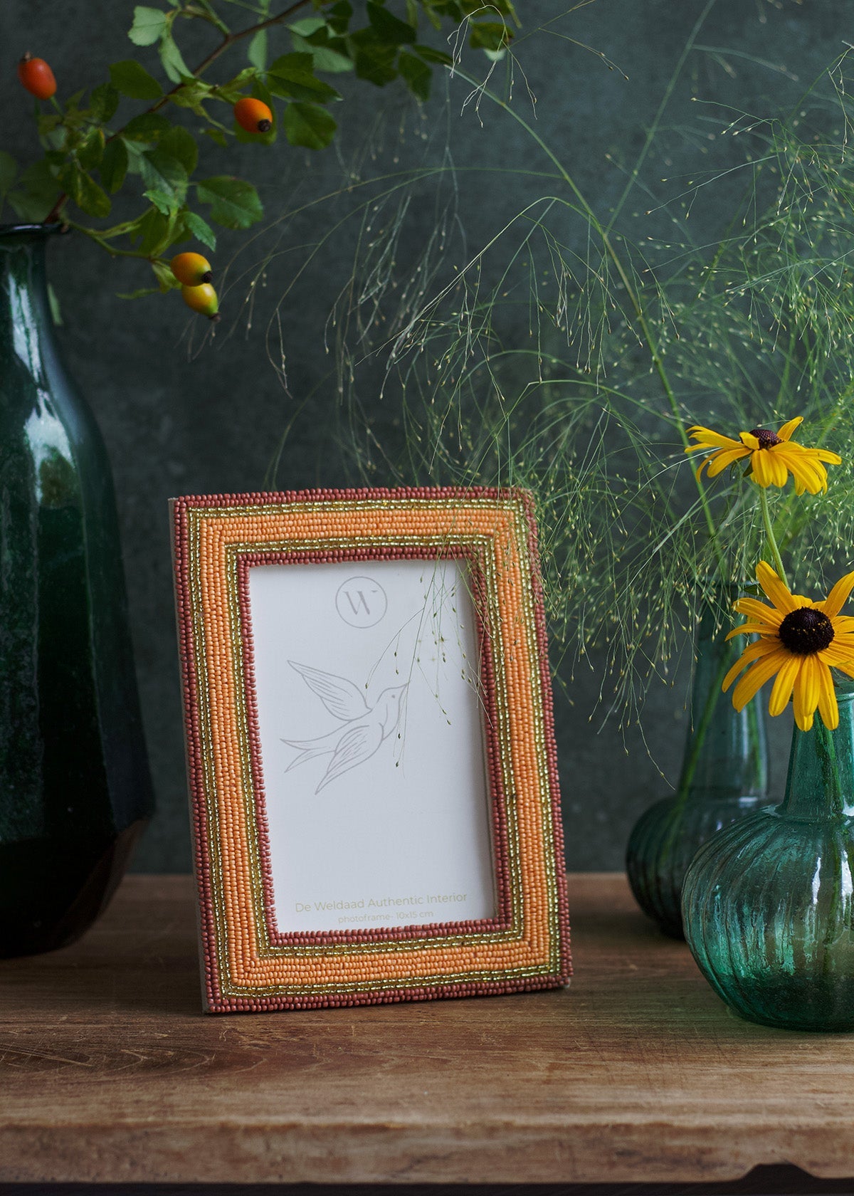 Decorative photo frame with a floral arrangement and vases on a wooden surface.