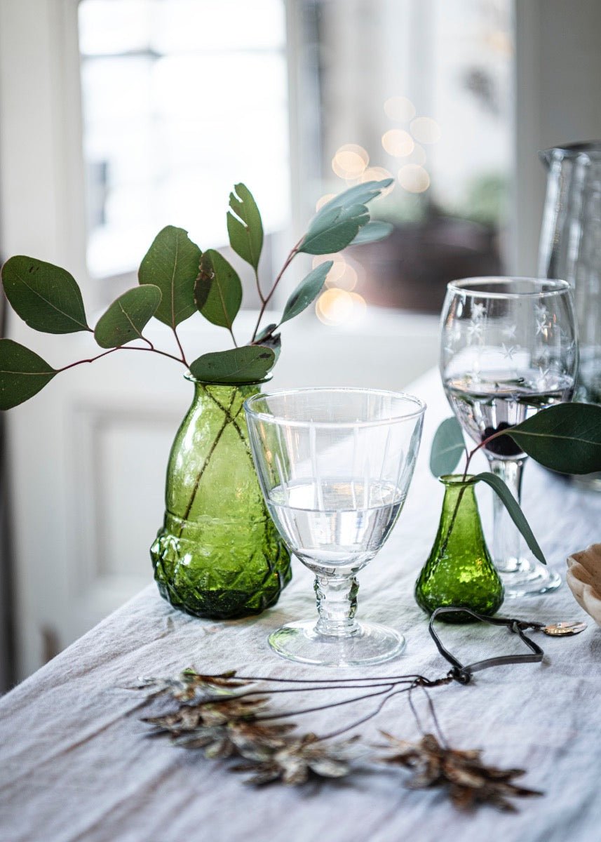 Transparent wineglass decorated with green vases & leaves on a white surface