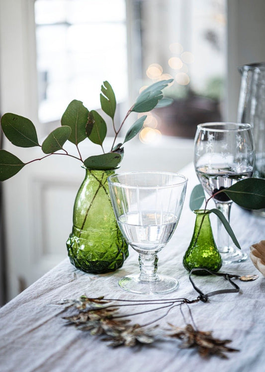Transparent wineglass decorated with green vases & leaves on a white surface