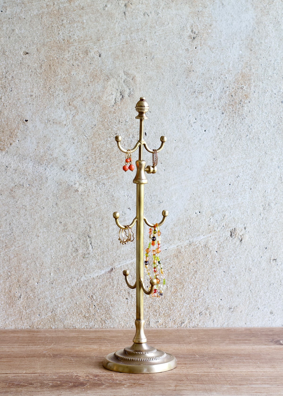 Brass jewelry stand with hanging earrings on a wooden surface and light gray background