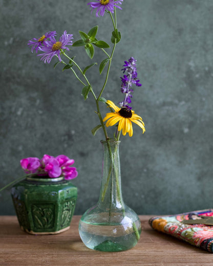 Clear glass vase with purple and yellow flowers on a wooden surface against a gray background