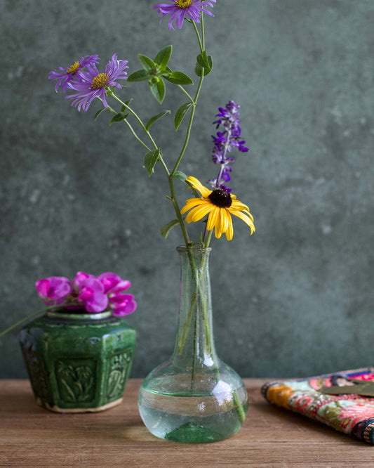Clear glass vase with purple and yellow flowers on a wooden surface against a gray background