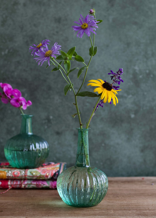 Green ribbed vase with flowers on a wooden surface against a dark background