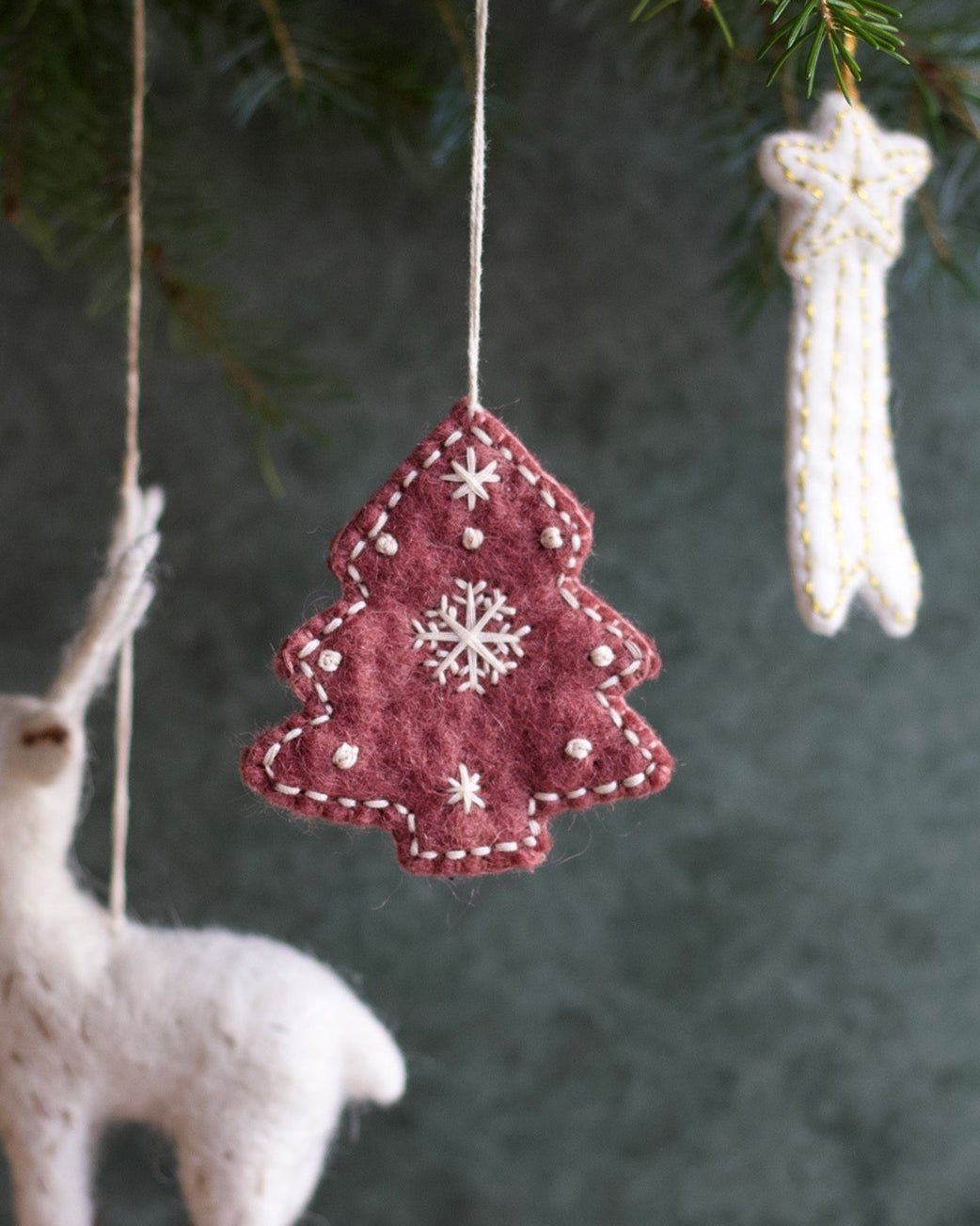 Felt Christmas tree ornament with snowflake design hanging from a branch.