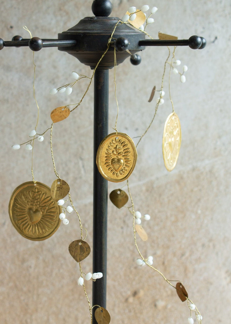 Handmade brass heart medallions hanging from a golden garland with white bead accents.
