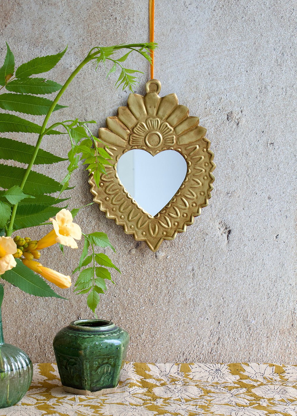 Decorative heart-shaped mirror with floral and vase on a textured wall