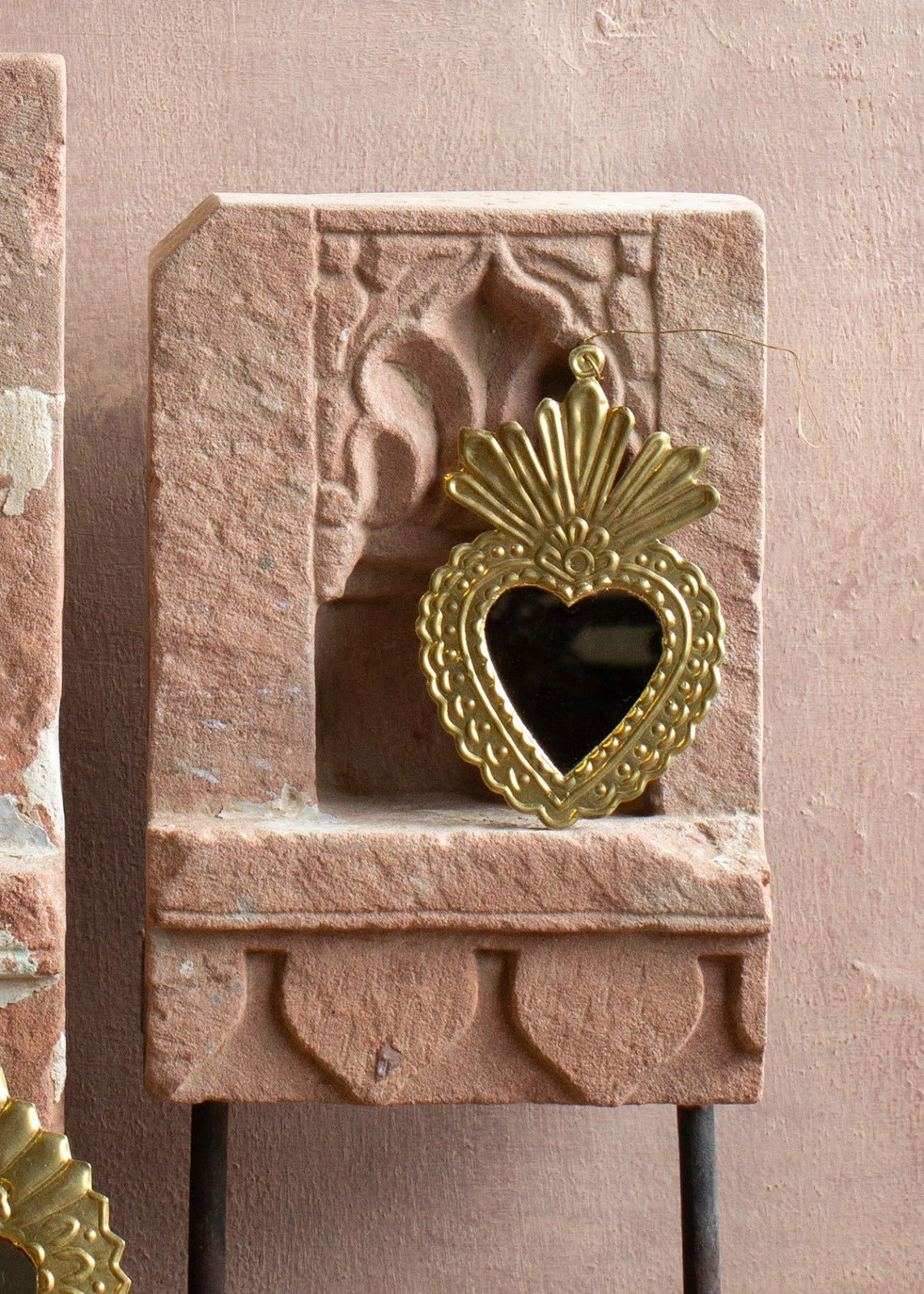 Brass ex-voto ornament with a small heart-shaped mirror and embossed details, displayed against stone.