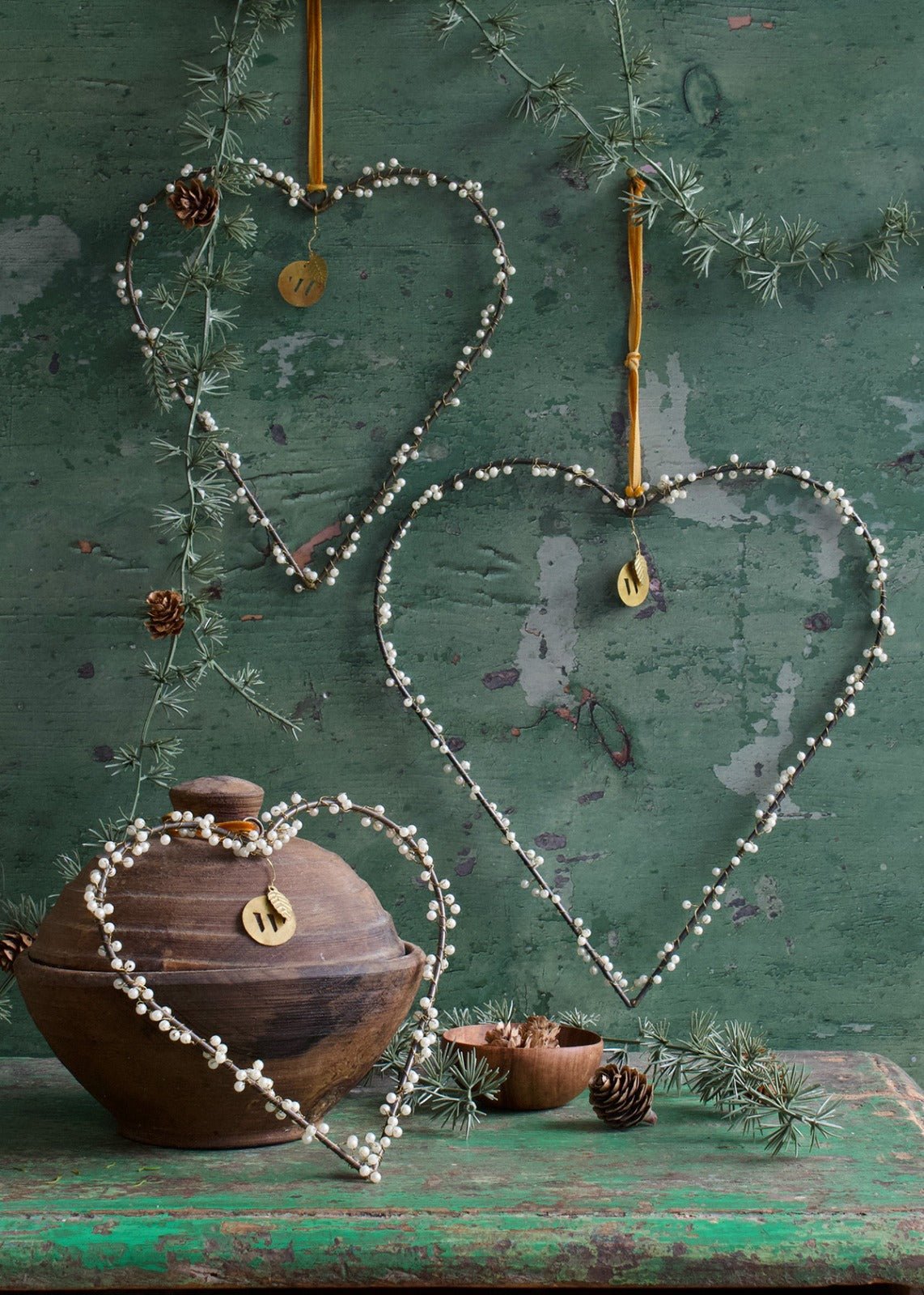 Set of three heart-shaped ornaments with pearl beads on green rustic background