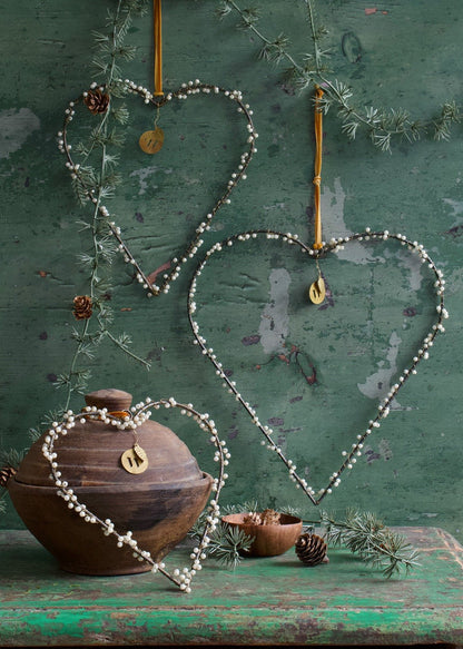 Set of three heart-shaped ornaments with pearl beads on green rustic background